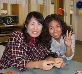 two students smiling for a photo while doing origami
