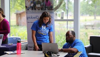 a male and a female looking at a computer screen wearing madonna university shirts
